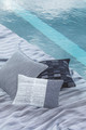 Umbra Perennials® Performance Weave by Ismini Samanidou, featuring a durable dark indigo Ikat design, shown behind the cushions. Water-resistant and ideal for both poolside and outdoor upholstery.